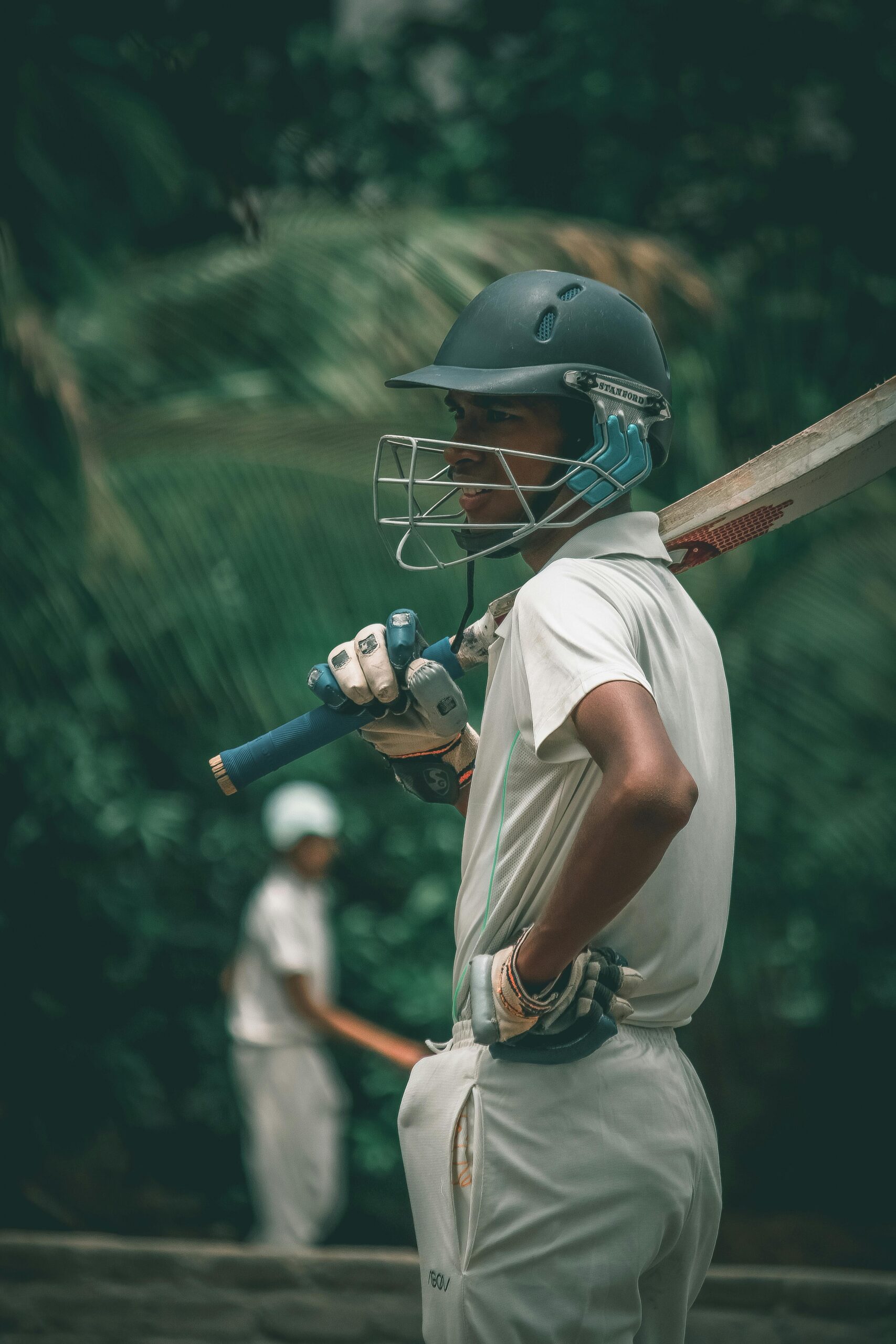 A focused young male cricket player with helmet and bat, ready for the game on an outdoor field.